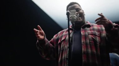 Stüdyoda şarkı söyleyen bir şarkıcının düşük açılı çekimi. Siyah arka plan ve yukarıda parlak ışıklar var.