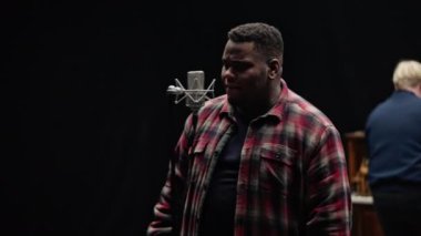 Kamera, bir adam arkadan piyano çalarken duygusal olarak mikrofona şarkı söyleyen bir şarkıcının önünde hareket eder.