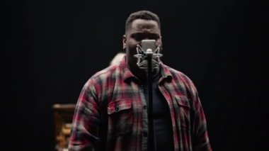 Karanlık bir arka planda duygusal bir şarkı seslendirirken parmaklarını gösteren bir şarkıcının yakın plan çekimi.