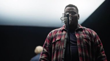 Düşük açı, bir adamın göğsüne dokunurken karanlık arka planı olan bir stüdyoda duygusal olarak bir mikrofona şarkı söylerken görüntüsü.