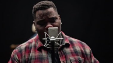 Mikrofon standını tutan ve bir şarkıyı seslendirdikten sonra kameraya bakan bir adam resmi.