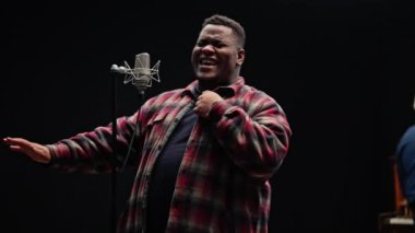 Bir şarkıcı ve piyanist, siyah arka planlı bir stüdyoda yoğun bir performans sergiliyor.