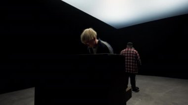 Yavaş çekimde bir piyanist ve bir şarkıcının siyah arka planlı bir stüdyoda arka arkaya sahne almaları.