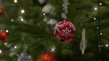Kırmızı ve beyaz kar tanesi topuna odaklanmış, bulanık incik boncuklar ve ışıklar noel ağacında asılı.