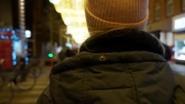 一个身穿粉色燕尾服和冬季夹克的女孩走在有圣诞灯的人行道上的背景照片 — 图库视频影像