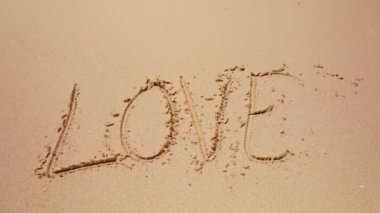 Aşk sözcüğü, kumsalın kumlu sahillerinde akan sular tarafından silinir.