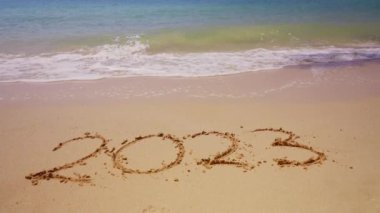 Deniz dalgaları 2023 'ü silip süpürüyor. Plajın kıyısında yazıyor.
