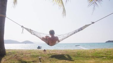 Yavaş çekimde uzaklaşın. Tayland 'da gündüz vakti deniz kenarında sallanan bir çocuğun arka görüntüsünü gösterin.