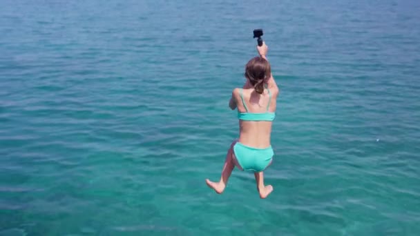 在泰国的一个海滩上 一个拿着手提式动作相机的女孩慢吞吞地跳到蓝色的水里 — 图库视频影像