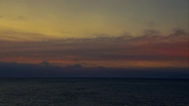 İzlanda 'da gün batımında, denizin sakin sularını ve ufuktaki dağların siluetini gösteren bir tava görüntüsü.