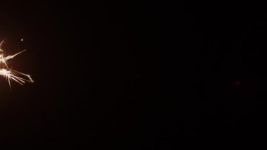 Çerçevenin sol tarafında koyu bir zemine karşı yanan altın maytap.