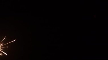 Çerçevenin sol alt tarafında koyu bir zemine karşı yanan maytap.