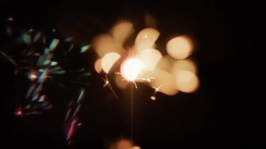 Çerçevenin sol tarafında koyu yeşil ve pembe ışıklar bulunan yanan bir maytaptan çıkan Bokeh ışıkları koyu arkaplana karşı.