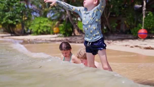 タイの昼間 若い男の子が次の波に飛び込む間 ビーチに座っている子供たちの幅広いショット — ストック動画