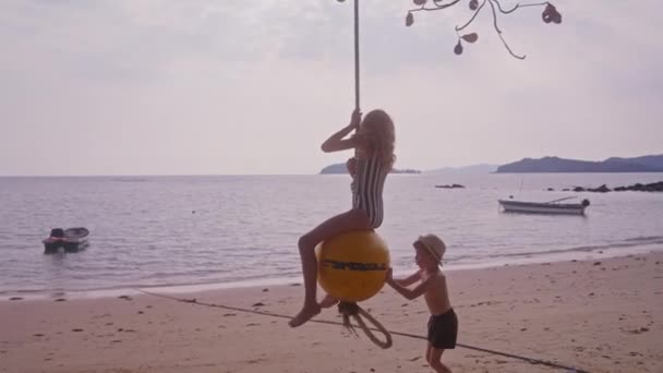 一段录像显示 一个男孩白天在泰国海滩上推着一个女孩骑着浮标球荡秋千 — 图库视频影像
