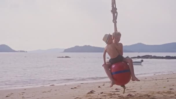 在泰国 两名男孩白天骑着浮标球在海滩上荡秋千的录像 — 图库视频影像