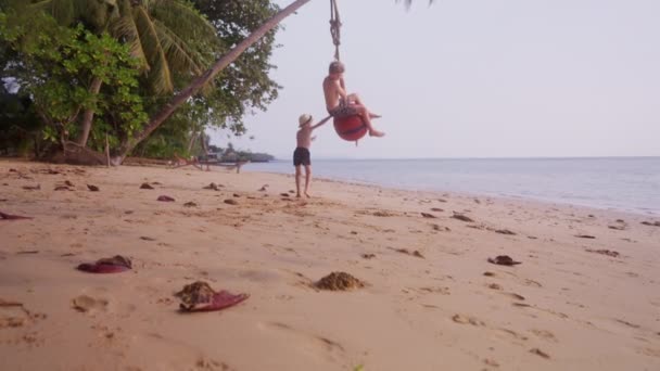 一段录像显示 一个男孩推着另一个男孩骑着浮标球 白天在泰国海滩上荡秋千 — 图库视频影像