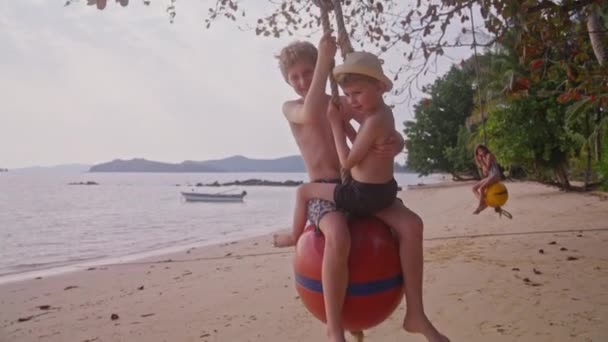 一个视频中 两个男孩在一个浮标球秋千上荡秋千 一个女孩也在后面荡秋千 在泰国的一个海滩上 — 图库视频影像