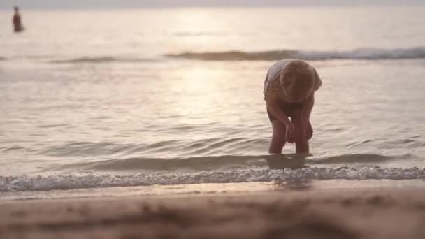 一个男孩在日落时试图沿着海滩的海岸线去找沙子时往下看的视频 — 图库视频影像