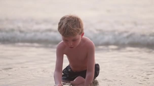 タイにあるビーチの海岸線に沿って海水を見ている少年の中型ショット — ストック動画