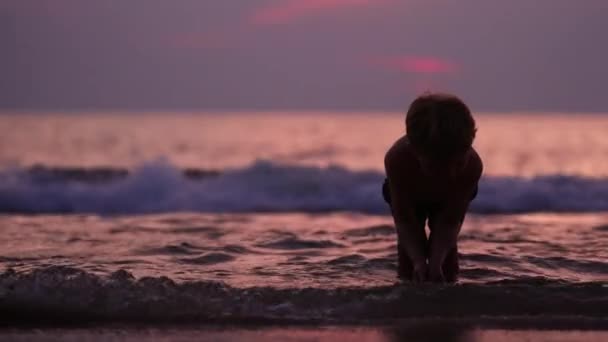 日没の間にタイのビーチの海岸線に沿って水で遊んでいる少年のビデオ — ストック動画