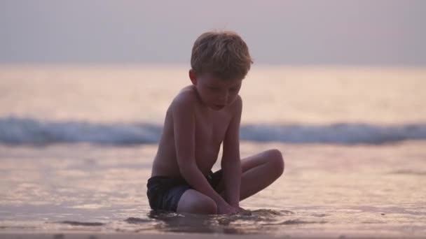 タイの日没時に砂と遊ぶビーチの海岸沿いの少年のビデオ — ストック動画