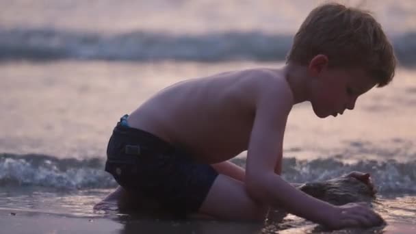 タイの日没時にビーチの海岸線に沿って砂を成形少年の側のビューを示すビデオ — ストック動画