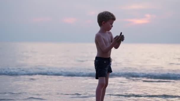 タイの日没時に海水で手にした砂を投げつける少年のビデオ — ストック動画