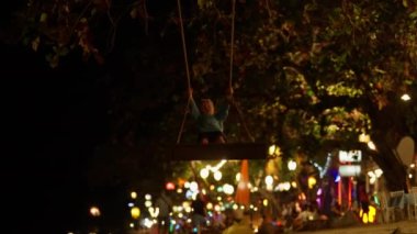 Tayland 'da gece vakti arkasında renkli ışıklarla salıncakta sallanan bir çocuğun geniş bir görüntüsü.