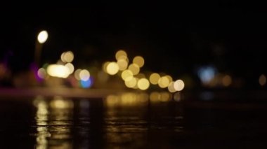Gece vakti Tayland 'da bir plajda arkasında sıcak Bokeh ışıkları olan dalgalanmaları gösteren bir video.