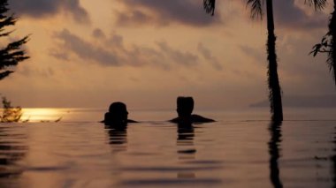 Tayland 'da gün batımında sonsuz havuzun kenarında bir kız ve erkek çocuğunun videosu.