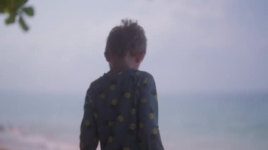 Tayland 'da gündüz vakti sahile bakan ve kumu işaret eden bir çocuğun videosu.