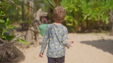 Bir heykelin üzerinde asılı duran çöp kutusuna doğru yürüyen ve plastik şişeyi içine atan bir çocuğun videosu.