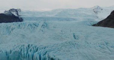 İzlanda 'daki engin mavi buzulların üzerinde yavaşça süzülen bir dronun görüntüsü.
