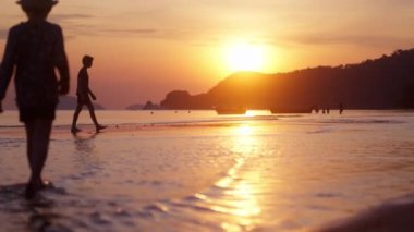 Tayland 'da gün batımında kumsalın ıslak kumlarında bir tekneyle yürüyen çocukların düşük seviyeli bir çekimi.