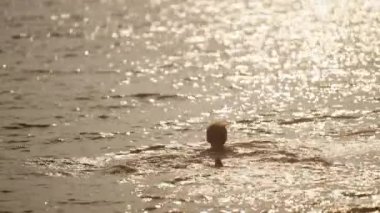 Bir çocuk gün batımında Tayland 'da kendisine doğru yürürken bir çocuğun deniz suyuna dalışının videosu.