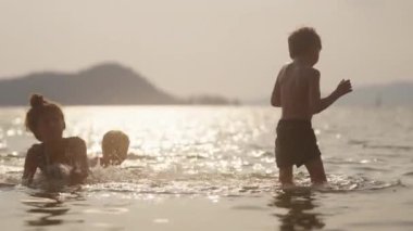 Ayağa kalkmaya çalışan ama kardeşleri de Tayland 'da gün batımında plajın keyfini çıkarırken sığ deniz suyuna düşen bir kızın videosu.