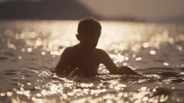 Gün batımında Tayland 'da bir plajda yüzen bir çocuğun videosu.