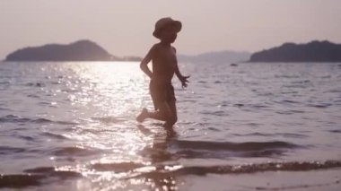 Gün batımında Tayland 'da bir plajda oynayan ve tekmeleyen bir çocuğun videosu.
