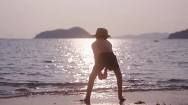 Gün batımında Tayland sahiline ıslak kum atan bir çocuğun videosu.