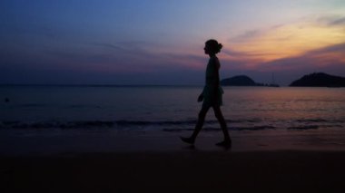 Gün batımında Tayland sahillerinde yürüyen bir kızın yan görüntüsü.