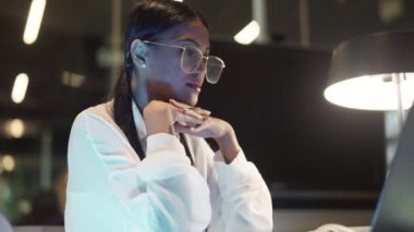 Bir kütüphanede projesini yaparken dizüstü bilgisayarına bakan at kuyruklu bir öğrencinin düşük açılı yan görüntüsü.