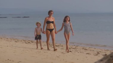 Çocuklarıyla birlikte Tayland 'da bir sahilde yürüyüş yapan bir annenin gündüz videosu.