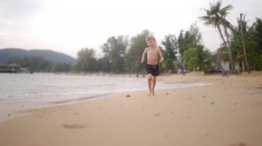 Tayland 'da bir sahilde koşan genç bir çocuğun gündüz videosu.