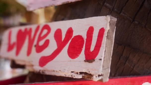 右から左へのクローズアップは タイのビーチで木の幹に投稿した愛という言葉で 赤と白の木製の看板を示しています — ストック動画