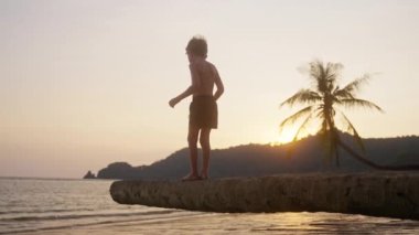 Ağaç gövdesindeki bir çocuğun Tayland 'da bir sahildeki deniz manzarasına baktığı bir video.