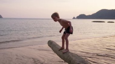 Gün batımında Tayland 'da bir sahilde ağaç gövdesinde oynayan bir çocuğun videosu.