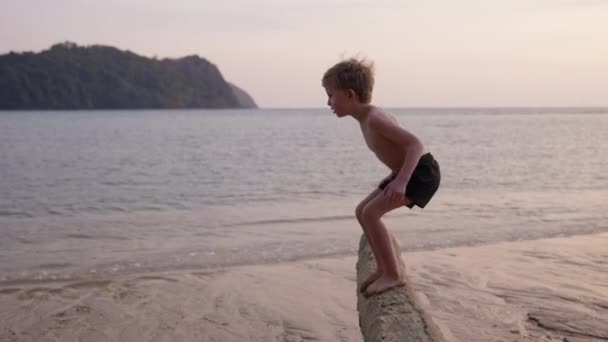 日没時にタイのビーチで木の幹を飛び回る少年のビデオ — ストック動画