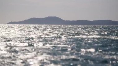 Tayland 'da bir gündüz videosu ufuktaki bir adaya karşı bulanık, pırıl pırıl okyanusu gösteriyor.