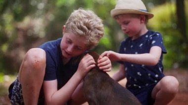 Tayland 'da gündüz vakti bir çocuğun yüzünü koklayan bir köpeği okşayan iki çocuk.